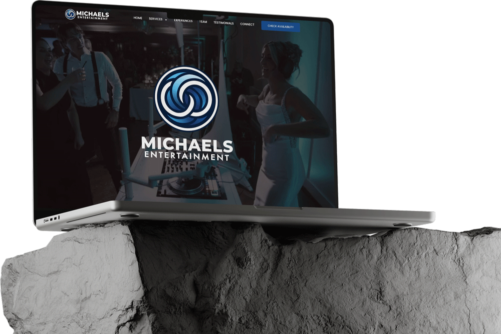 A laptop sits on a large rock slab, displaying the Michaels Entertainment website. The screen shows an event scene in blue lighting, with a large company logo and navigation menu—perfect for showcasing expert Website Builds or Edit Website services.