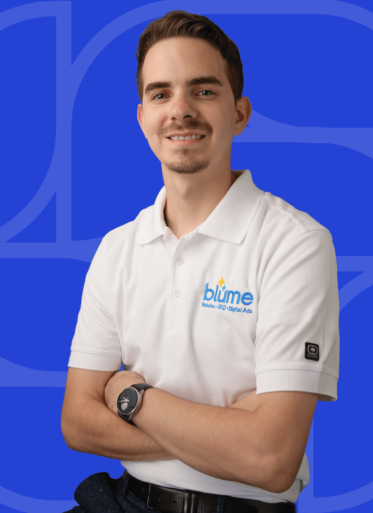 A young man with short brown hair and a trimmed beard stands smiling with arms crossed. Peyton Tillotson is wearing a white polo shirt with a "blume" logo and a black watch, in front of a blue geometric background.