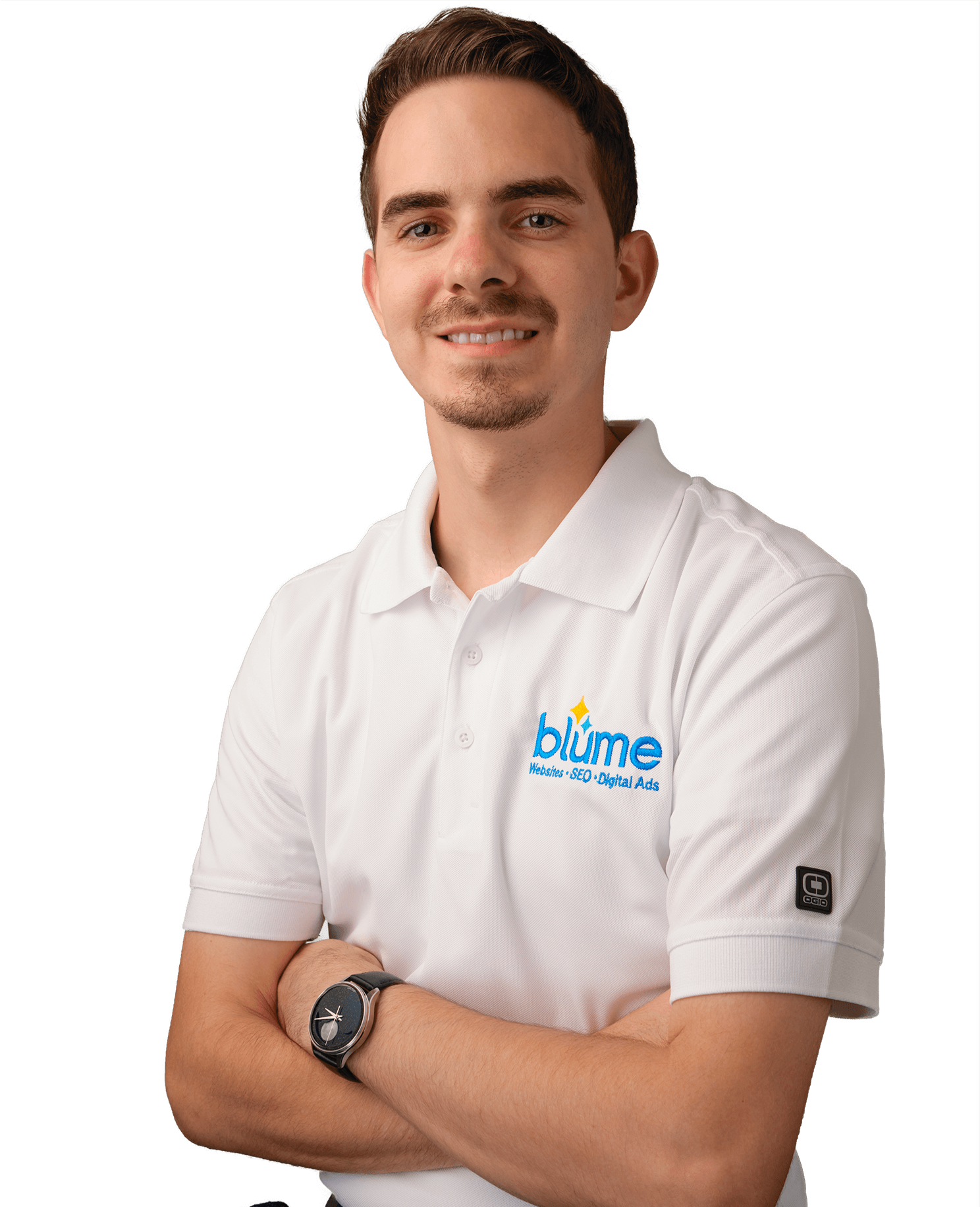 A man with short brown hair and light facial hair stands with arms crossed, wearing a white polo shirt with a "blüme Website - App - Digital Ads" logo and a black smartwatch. He is smiling and facing the camera.