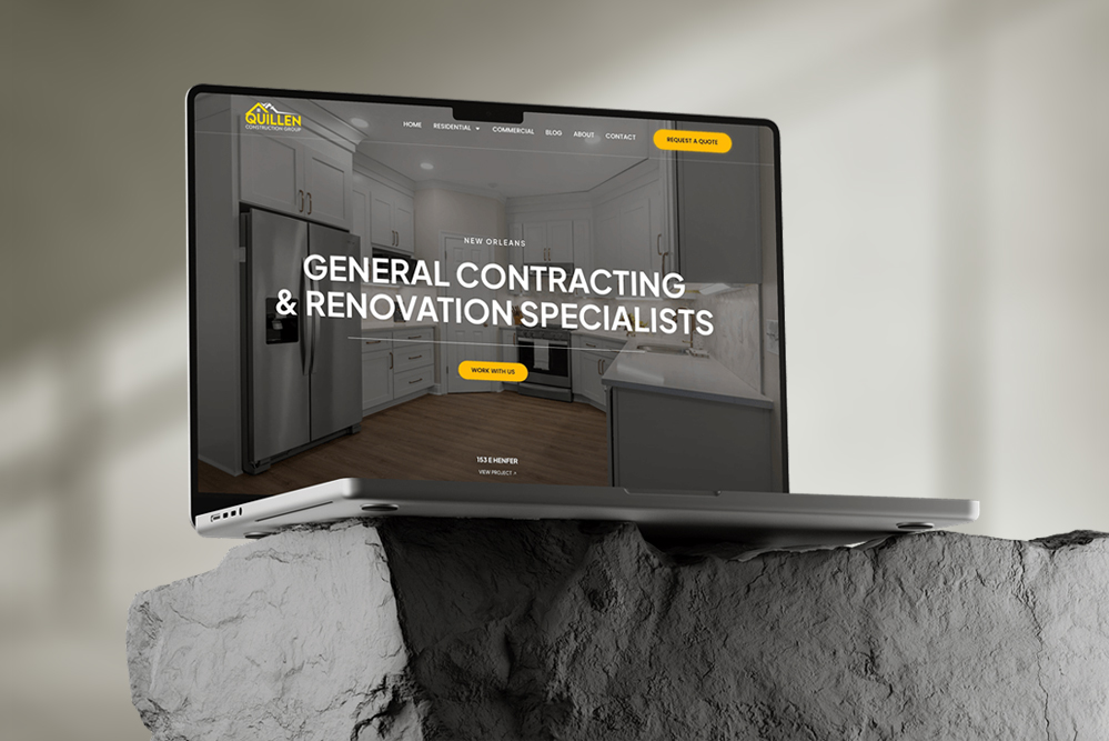 A laptop displaying a custom website for Guillen Construction, featuring a kitchen photo and the text “General Contracting & Renovation Specialists.” The laptop rests on a rough, gray stone surface with neutral lighting.