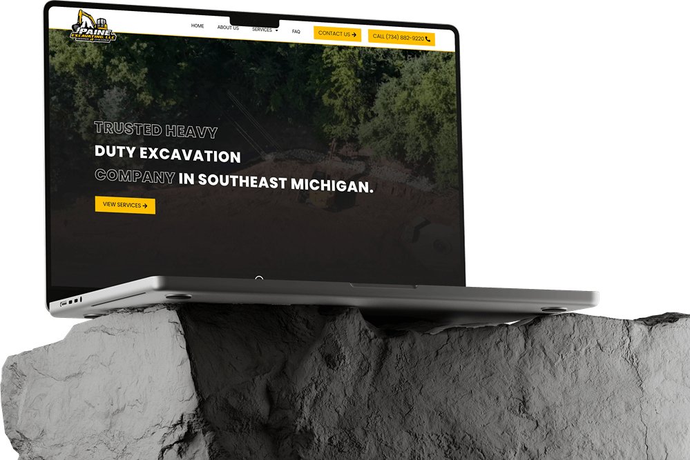 A laptop showcasing a heavy-duty excavation company’s website build in dark mode sits atop a large, rough rock against a plain white background.